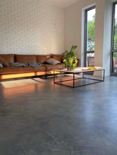 Mikrozement Boden Moderne Wohnzimmer mit einem braunen Sofa, Tisch und Pflanzen bei Tageslicht.