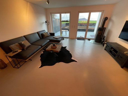 Mikrozement Boden Moderne Wohnräume mit Zementboden, einer Couch, Couchtisch und großen Fenstern.