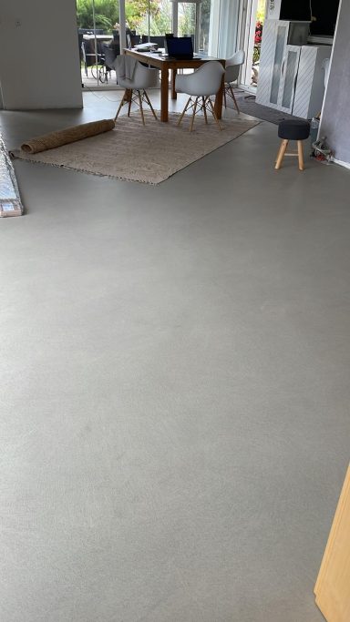 Mikrozement Boden Heller Boden mit einem Tisch und einem Stuhl im Hintergrund.